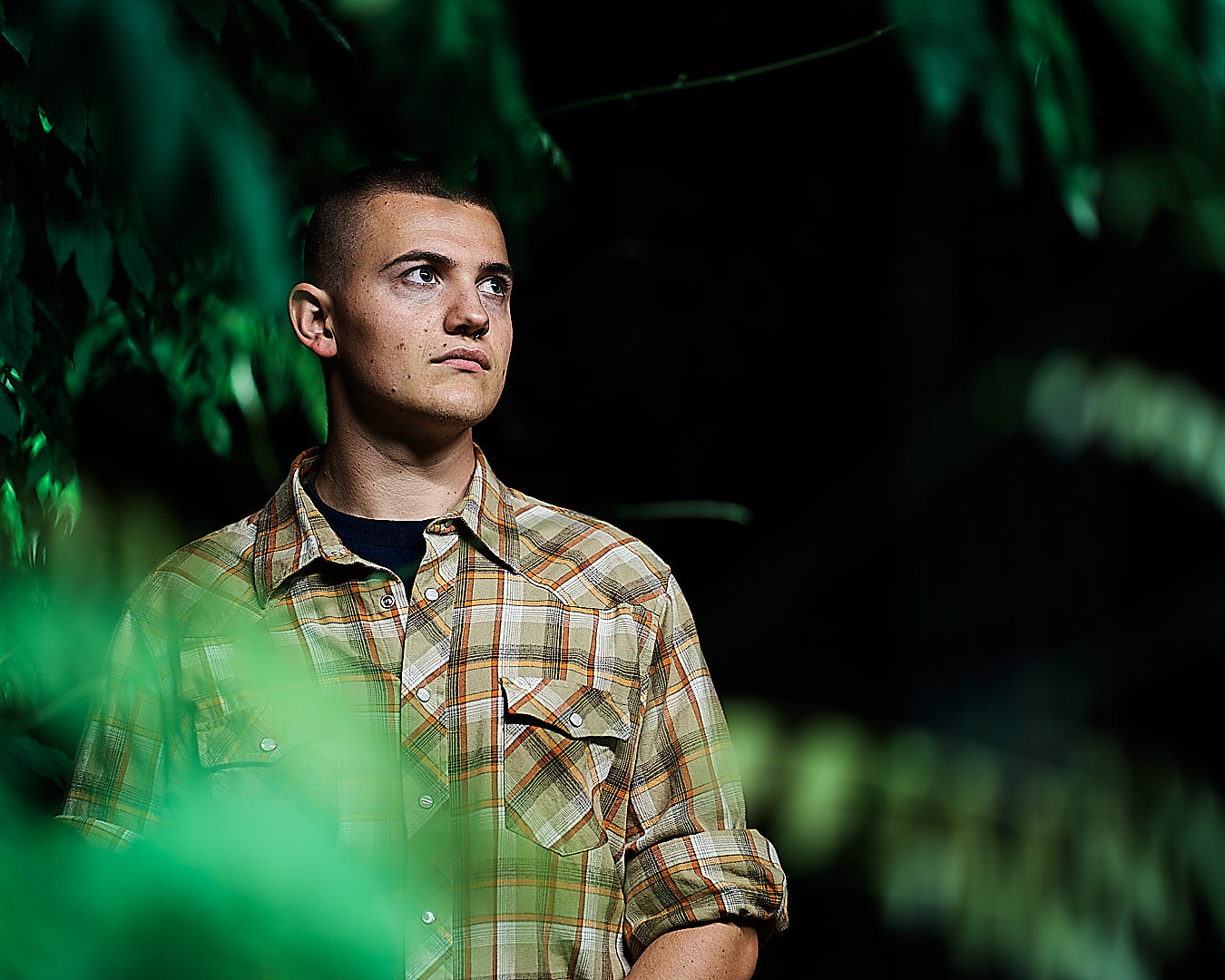 man standing between trees and leaves. he is looking into the far distance.