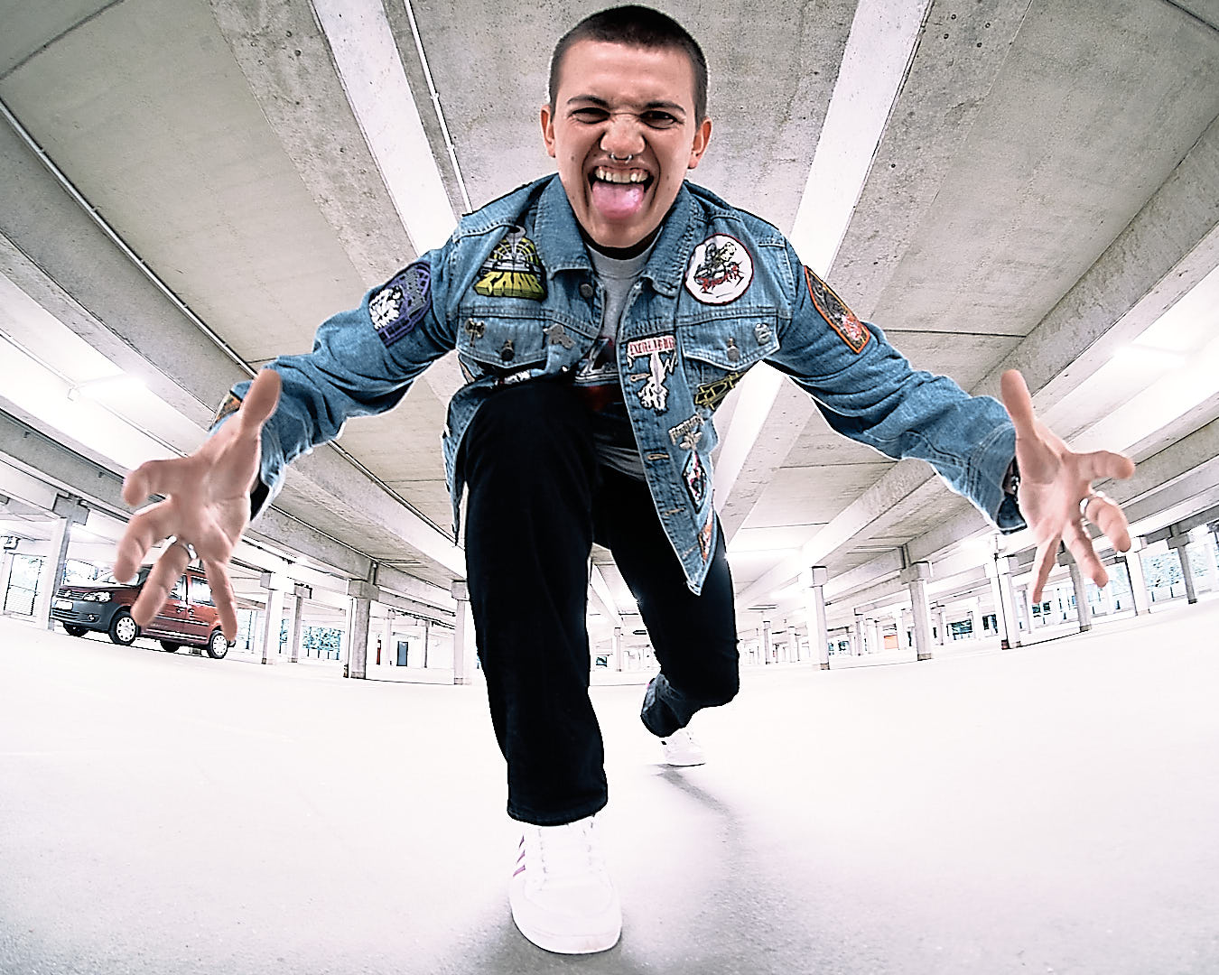 boy making funny face while stepping toward the camera. he is in a parking garage and has a nose ring